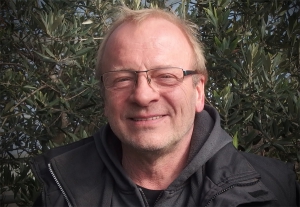 Portraitfoto Gerhard Glöckner in Arbeitskleidung, im Hintergrund grüne Pflanzen