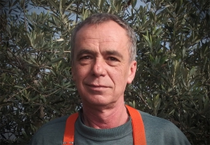 Portraitfoto Heinz Rudolf in Arbeitskleidung, im Hintergrund grüne Pflanzen